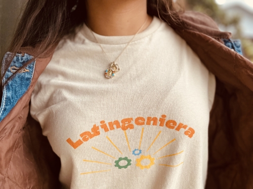 Close up of T Shirt on someone that reads "Latingeniera" in a bold orange font and colorful gears below it.