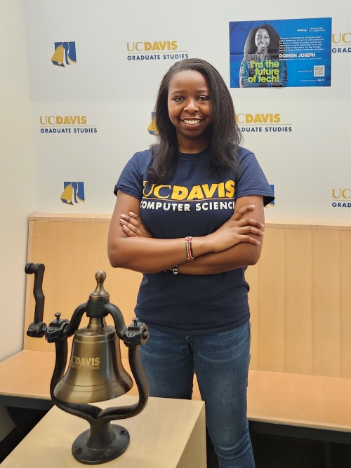 Doreen Joseph standing next to a copper bell and in front of a poster of herself