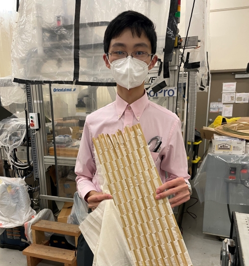 Shuhao Wan stands in lab holding cheese cloth and bamboo reeds