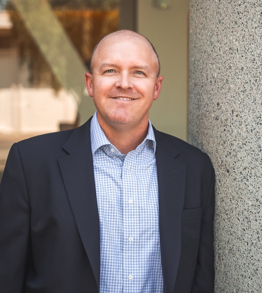 Kent Leach wearing a suit jacket and poses outside near a building