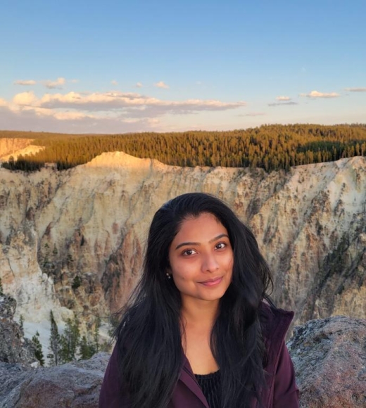 Portrait of Meera outside in a rocky landscape with trees and a canyon in the background