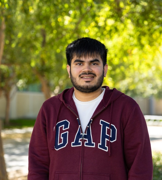 Ph.D. student in computer science Yash Vekaria stands outdoors wearing a GAP hoodie