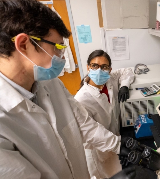 Two professors in lab coats speak over a microscope