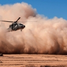 Helicopter emerging from a dust cloud against a blue background