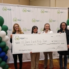 Two UC Davis students and two professors hold big check up in front of a step and repeat with AlgaePrize logo in green and white
