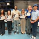 Six people stand for a group photo, five of them hold up certificates