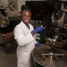 Laudia Anokye-Bempah stands in front of a coffee roaster