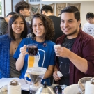 Three students hold up coffee cups in Coffee Center Lab