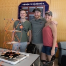 Three people posing for a picture behind a building structure display