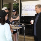 Dean of UC Davis Engineering Richard Corsi outside talking with people at an alumni event. In the background there is a Welcome Engineering Alumni sign with the UC Davis COE logo.