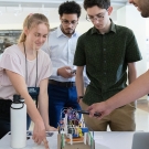 Students gather indoors and work on a project that is sitting on a table