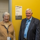 Brian Horsfield and his wife pose in front of a green wall and sign with their name