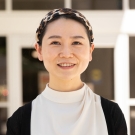 Jane Gu wearing a white blouse and black cardigan standing outdoors near a building on the UC Davis campus