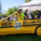 A child sitting inside a yellow car replica that says "UCD EcoCAR"