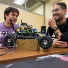 Erik Contreras and other student smile as they look at robotic car on table