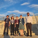 Five UC Davis engineering faculty and students standing in front of a stadium with blue sky and clouds behind them