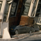 A car crushed by a sunken, tilting house. 