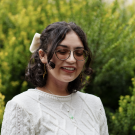 Estaina smiling in front of green bushes