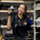 Pham in black polo holding DSLR in an equipment storage room