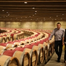 Two people stand in a circular room with hundreds of barrels of wine spiraling around