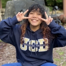 Portrait of Tichada Tantasirikorn making piece signs with their hands and wearing a UC Davis sweatshirt, outdoors