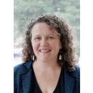 Jennifer Teerlink with curly hair, wearing a blue jacket, in a bright, natural setting.