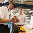 One person wears augmented reality goggles while another stands close by near a poster and interactive activity