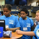 Three students stand together, looking at a laptop