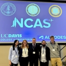 Five people standing under a blue projection screen with the NCAS logo