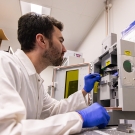 Calum Shelden wears PPR and works in a lab with a large microscope