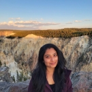 Portrait of Meera outside in a rocky landscape with trees and a canyon in the background