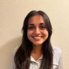 Aaleesha Doshi with long dark hair, wearing a striped button-up shirt