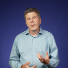 Simon Cherry against a blue gradient background in a filming studio
