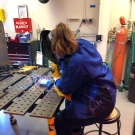 Person sitting at a welding table with sparks flying off machinery