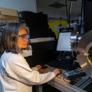 Yayoi Takamura, professor and chair of materials science and engineering wears safety goggles and a lab coat and stands near a machine in her lab