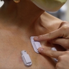 Person's body with three white wearable devices on it, one being pressed down by two fingers