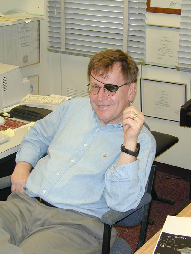 Middle aged man in an office with an eye patch and a blue shirt