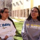 Twins in UC Davis sweaters sit outside near a building